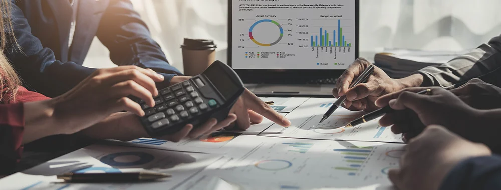 Business people are having a meeting and working towards balancing a budget with a calculator and computer. 